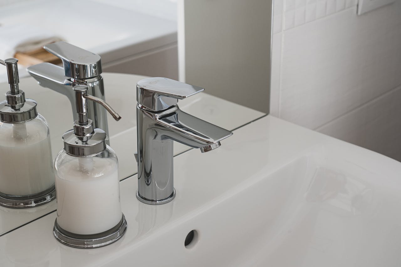 A sleek chrome faucet and soap dispenser on a pristine white sink in a modern bathroom setting.